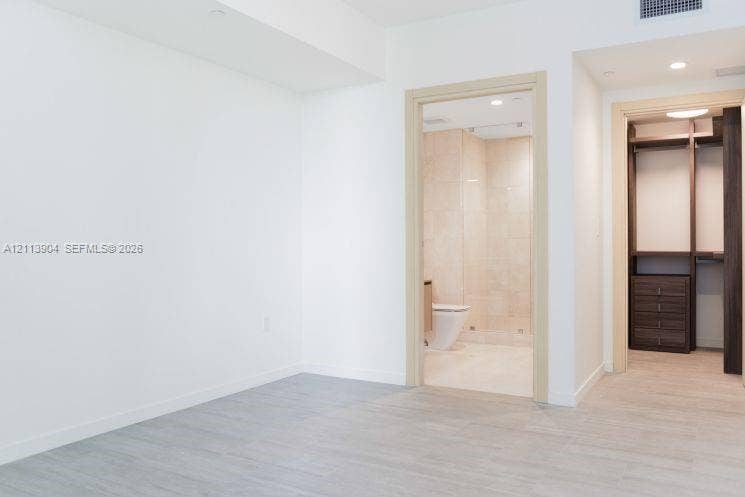 Light-toned wood-finish flooring, walk-in closet with built-in dark wood cabinetry, and recessed ceiling lighting