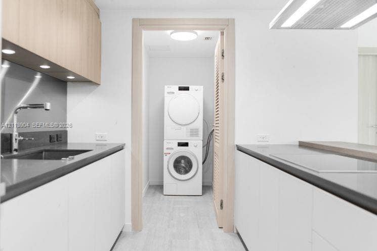 Kitchen area featuring flat-panel cabinetry, stone-surface countertops, under-cabinet task lighting, and a stacked laundry unit behind a louvered door