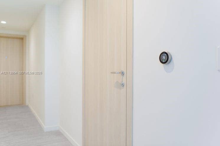 Light-toned wood-finish interior door featuring satin nickel hardware, paired with a wall-mounted smart thermostat and recessed ceiling lighting