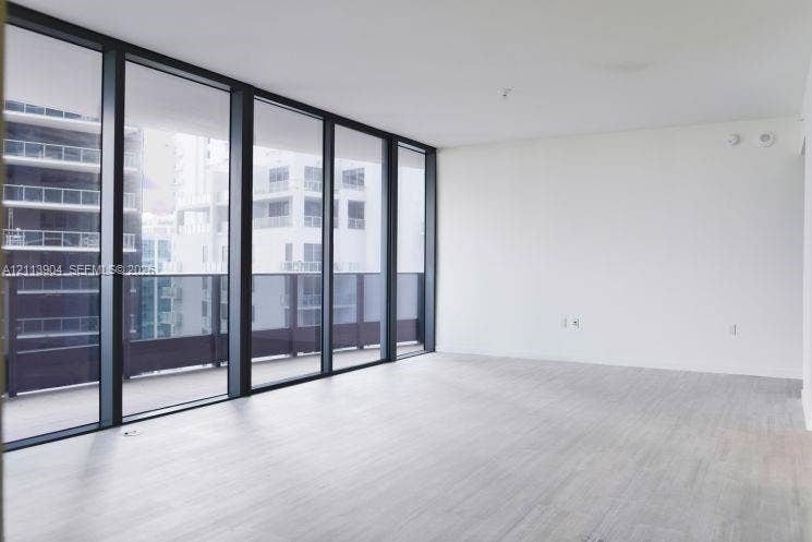 Floor-to-ceiling windows featuring dark frames, wood-finish flooring, and a glass-paneled exterior balcony