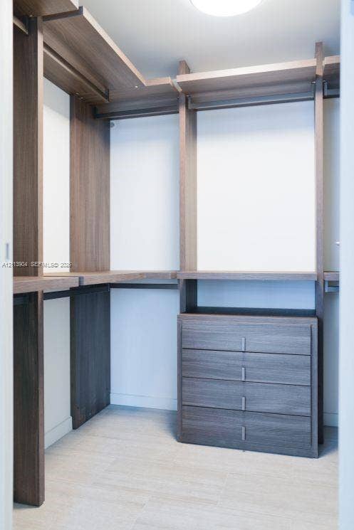Custom reach-in closet featuring wood-finish shelving, an integrated four-drawer storage unit, and brushed metal hardware