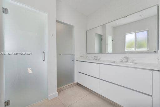 Bathroom featuring a dual-sink floating vanity with white cabinetry, a full-width wall mirror, oversized tile flooring, and frosted glass door enclosures