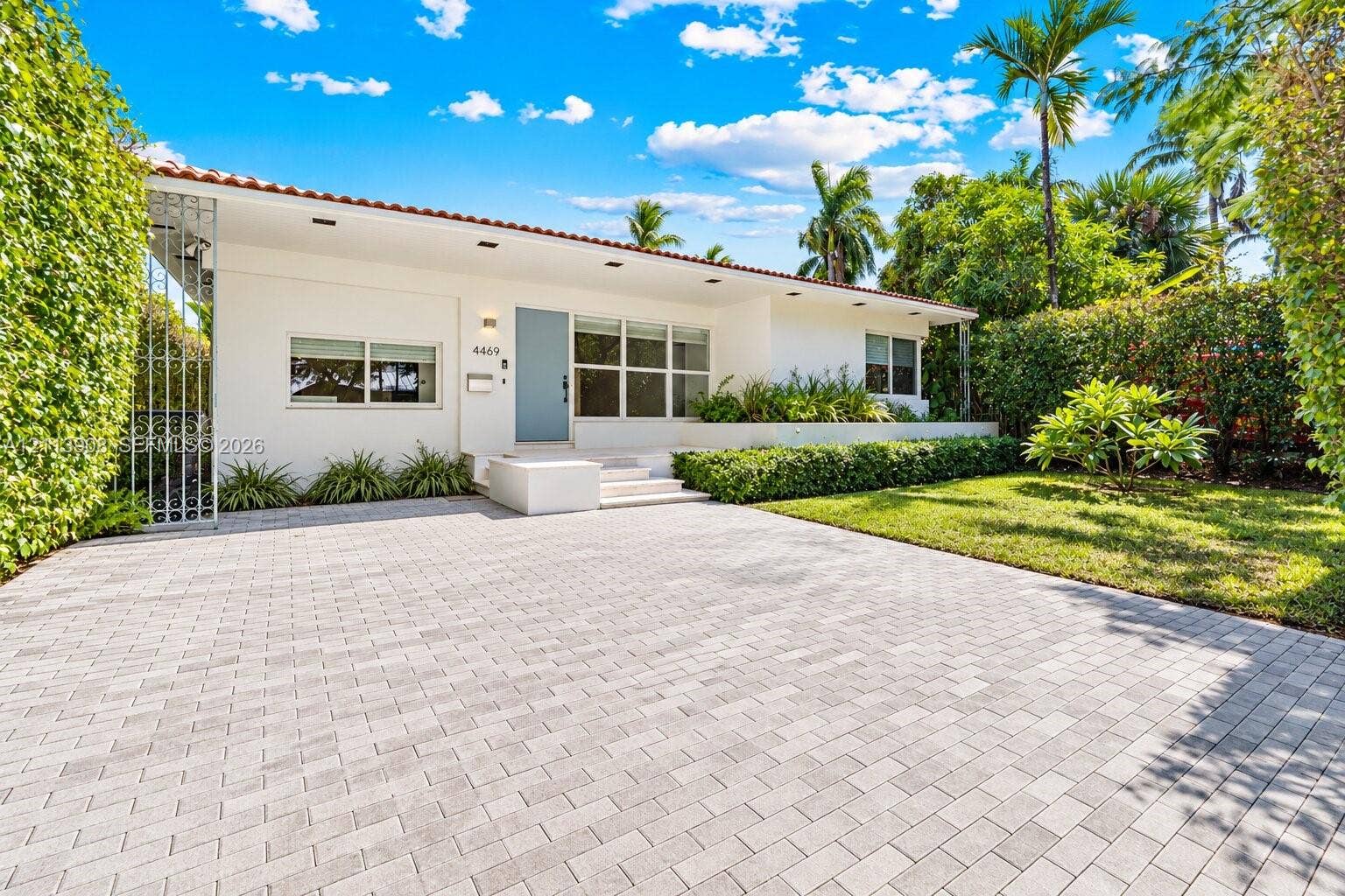 Single-story exterior featuring a paver driveway, concrete tile roof, manicured landscaping, and recessed exterior lighting