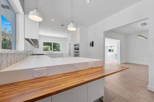 Kitchen featuring a waterfall-edge countertop, butcher block peninsula, geometric tiled backsplash, recessed lighting, and stainless steel built-in double wall ovens