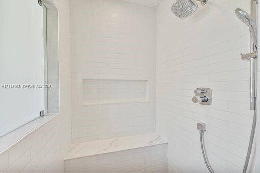 Walk-in shower featuring white subway-style wall tile, a stone-finish bench seat, an integrated wall niche, and dual-function polished chrome shower fixtures