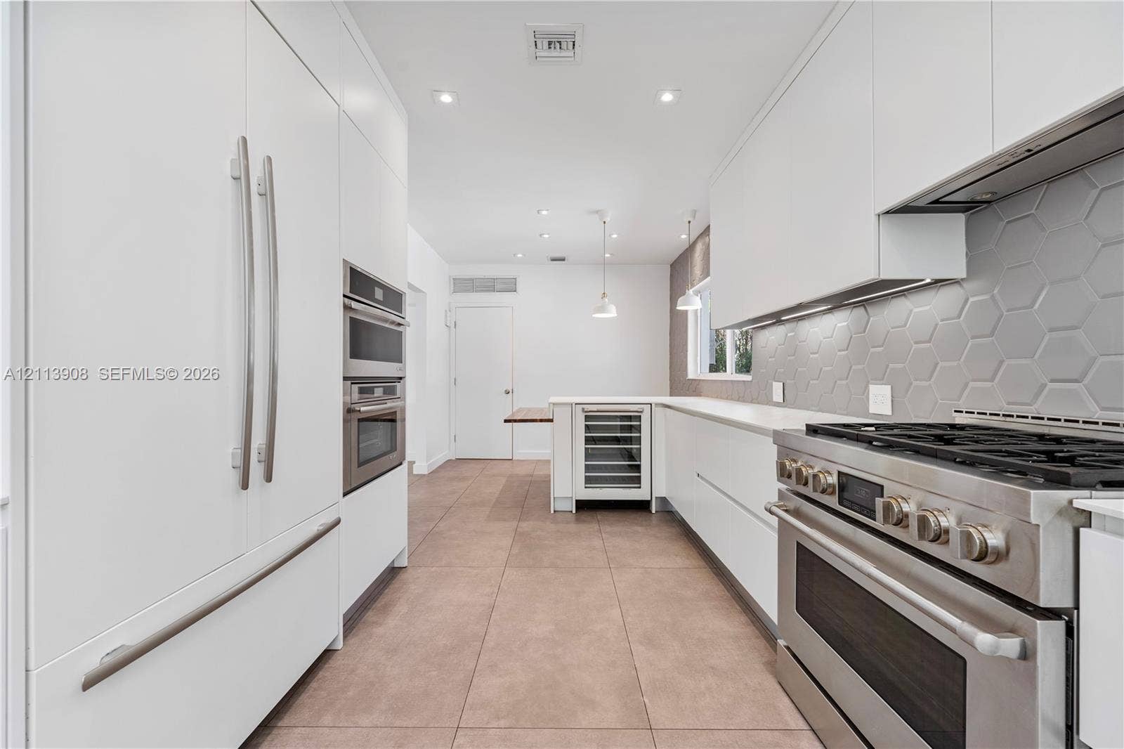 Contemporary kitchen featuring flat-panel white cabinetry, stainless steel professional-grade range, hexagonal tile backsplash, built-in wine refrigeration, and large-format tile flooring