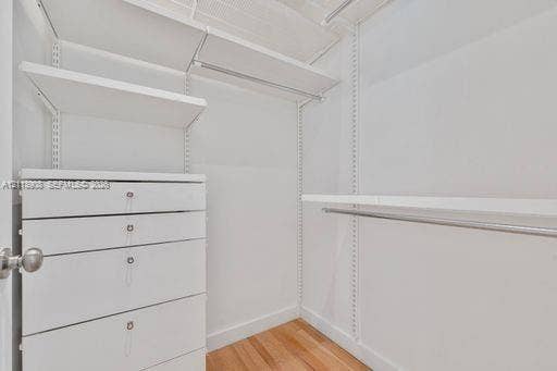 Walk-in closet featuring white built-in drawers, adjustable shelving, metal hanging rods, and wood-finish flooring
