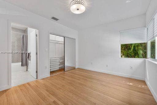 Room featuring wood-finish flooring, a decorative flush-mount ceiling light, a built-in closet with sliding mirrored doors, and window treatments