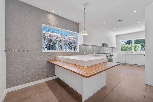 Kitchen featuring matte white flat-panel cabinetry, hexagonal-patterned accent wall, stone-topped island with wood-finished breakfast bar, and tile flooring