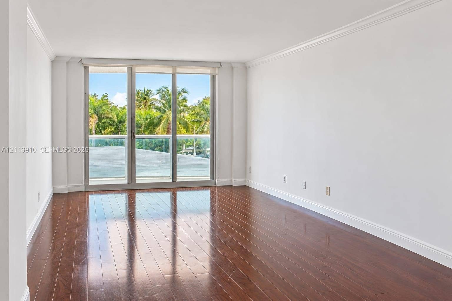 19380 Collins Avenue, #218, Sunny Isles Beach, FL 33160 Open-concept interior featuring wood-finish flooring, crown molding, and floor-to-ceiling glass sliding doors leading to a balcony with a glass railing