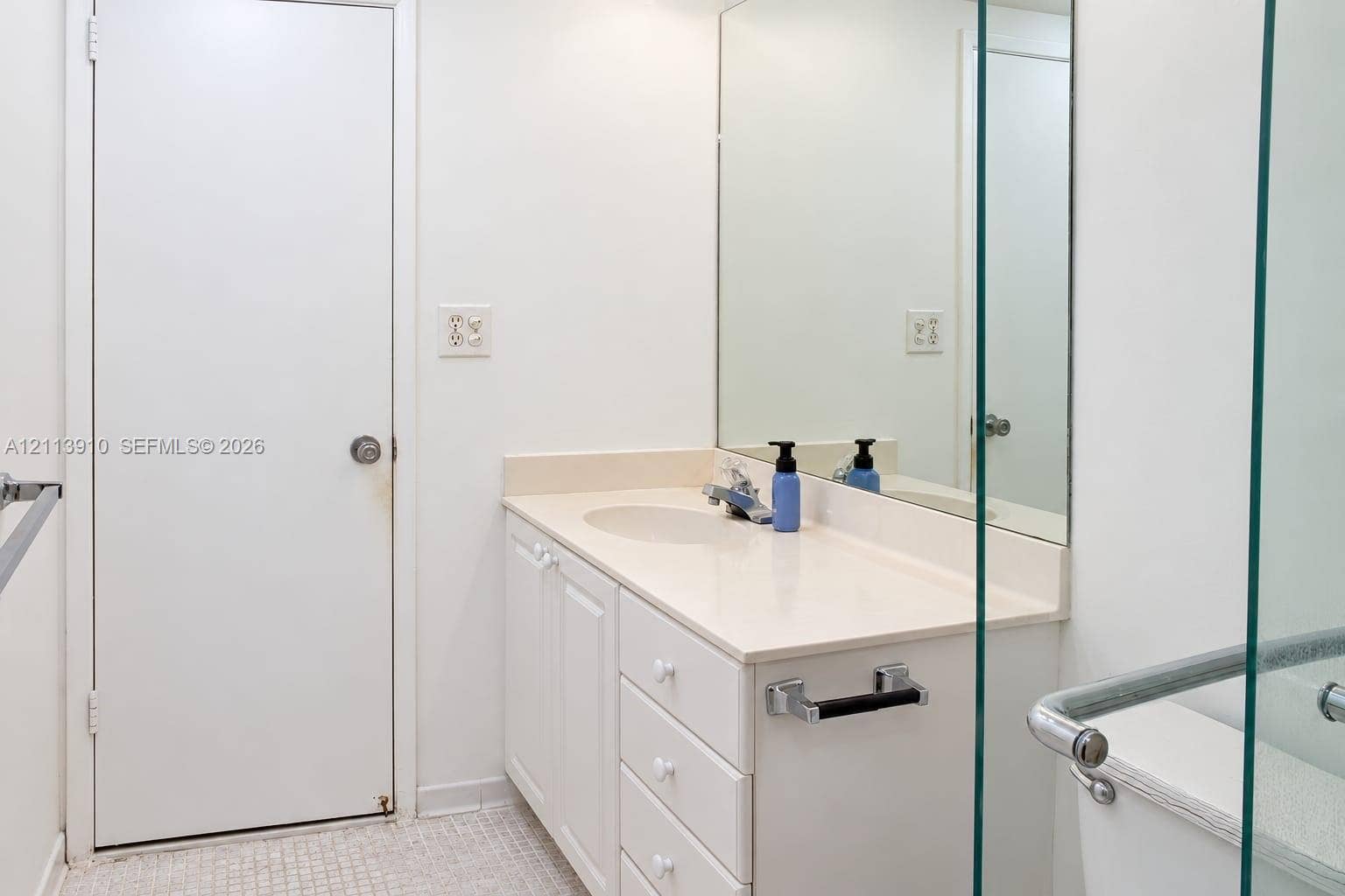 19380 Collins Avenue, #218, Sunny Isles Beach, FL 33160 Bathroom featuring a solid-surface vanity countertop, integrated sink, white cabinetry with drawers, large wall-mounted mirror, and glass-enclosed shower stall with a grab bar