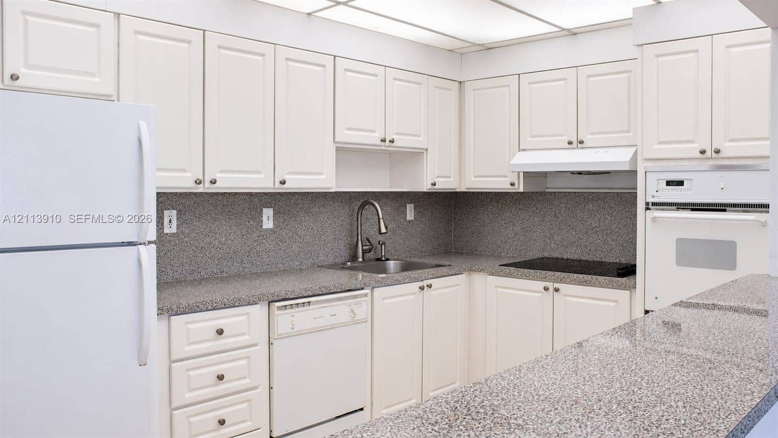19380 Collins Avenue, #218, Sunny Isles Beach, FL 33160 Kitchen featuring off-white cabinetry, speckled stone countertops, a stainless steel faucet, a built-in wall oven, and a drop ceiling with integrated lighting