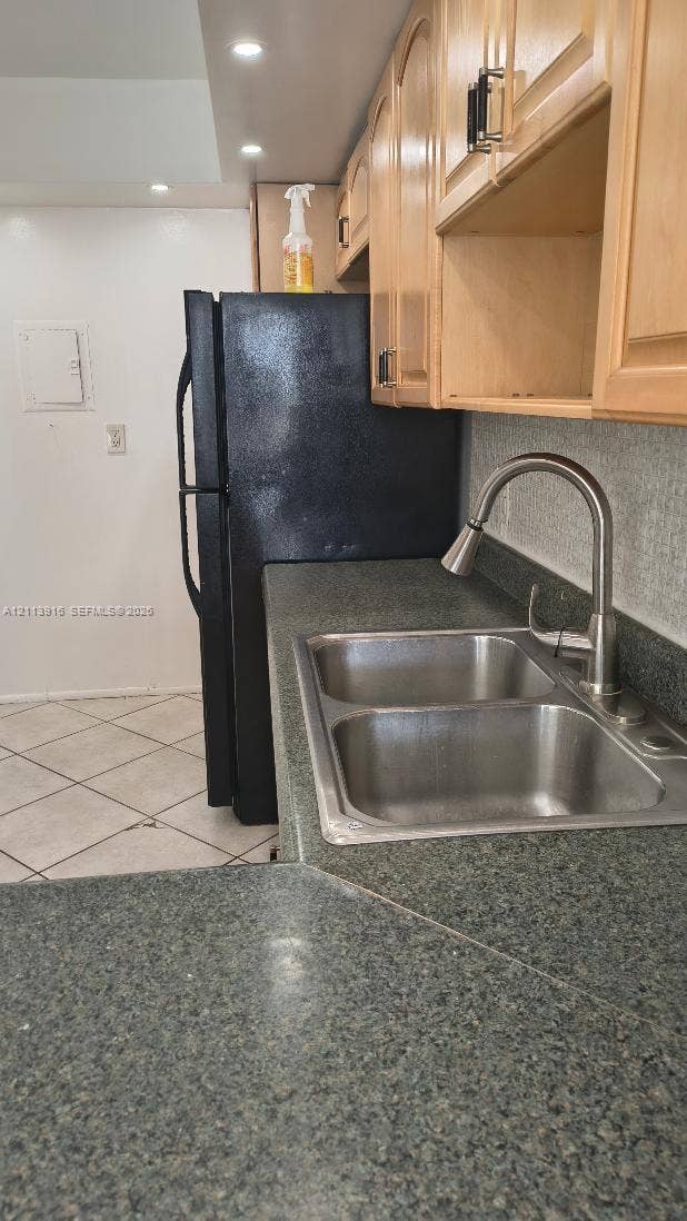 1301 Miami Gardens Drive, #1521 W, Miami, Miami, FL 33179 Kitchen featuring wood-finish cabinetry, stone-texture laminate countertops, a stainless steel double-basin sink with a pull-down faucet, a built-in black refrigerator, and tile flooring