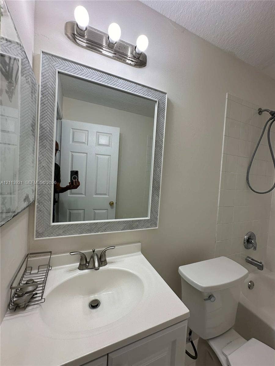 824 Summit Lake Drive, West Palm Beach, West Palm Beach, FL 33406 Bathroom featuring a vanity with a white countertop and oval sink, a wall-mounted mirror with a textured frame, a three-light vanity fixture, and a tub-shower combination with tiled surround