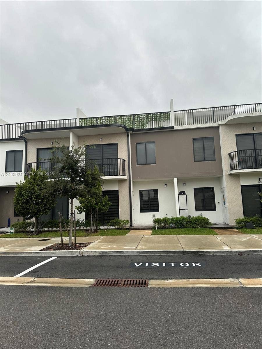 14569 SW 261st Terrace, #14569, Homestead, Homestead, FL 33032 Modern multi-level exterior featuring stucco siding, upper-level balconies with metal railings, a flat roof deck with perimeter fencing, and expansive glass sliding doors