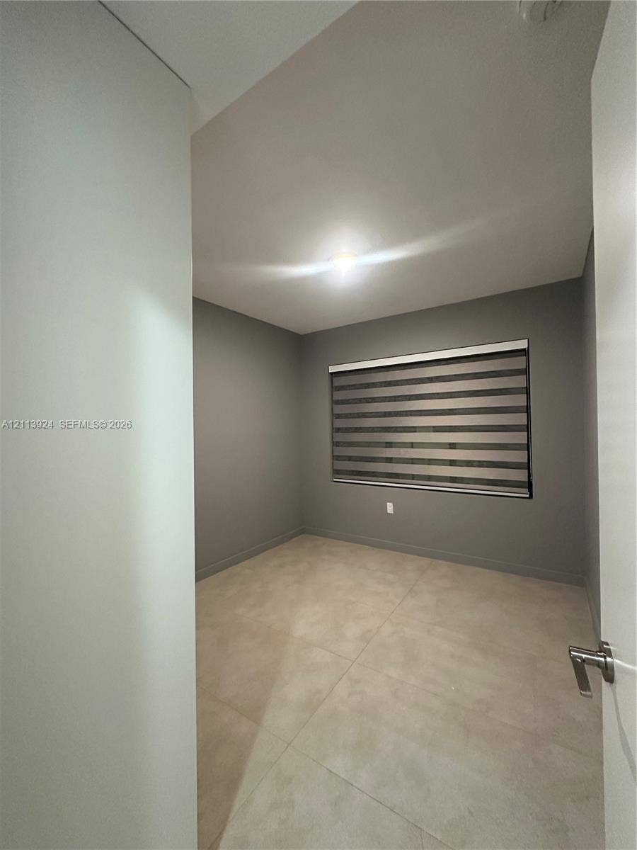 14569 SW 261st Terrace, #14569, Homestead, Homestead, FL 33032 Neutral-toned interior space featuring large-format tile flooring, grey wall finish, and a window equipped with horizontal zebra-style blinds