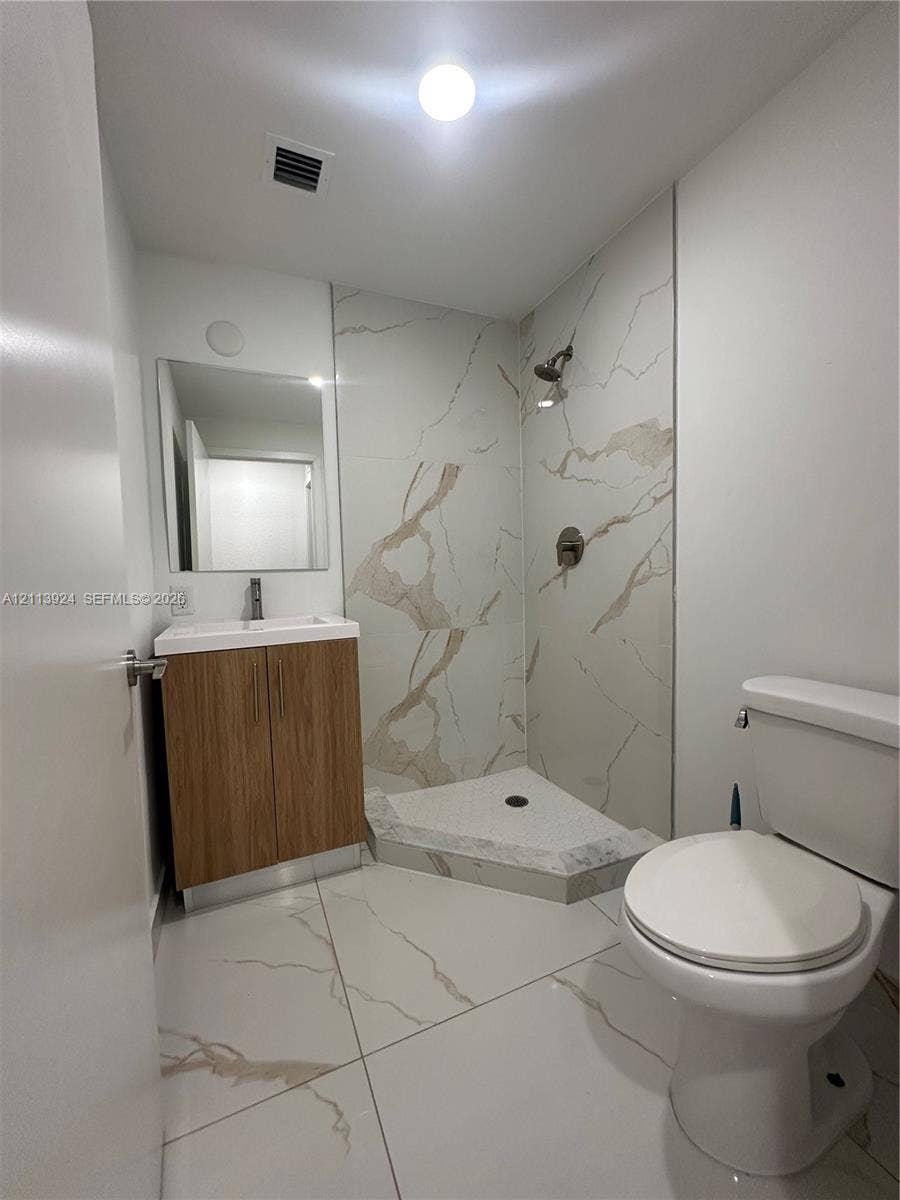 14569 SW 261st Terrace, #14569, Homestead, Homestead, FL 33032 Bathroom featuring large-format veined tile flooring, a wood-finish vanity with a white basin, a corner shower enclosure with tiled surround, and a wall-mounted mirror