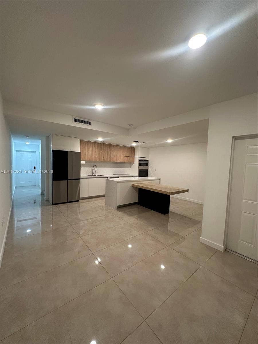 14569 SW 261st Terrace, #14569, Homestead, Homestead, FL 33032 Kitchen featuring high-gloss cabinetry, wood-finish upper cabinets, integrated stainless steel appliances, a center island with an attached breakfast bar, and polished tile flooring