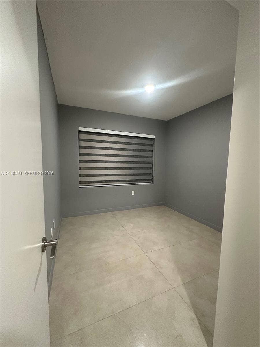 14569 SW 261st Terrace, #14569, Homestead, Homestead, FL 33032 Neutral-toned interior room featuring large-format tile flooring, gray walls, and a window equipped with banded roller shades