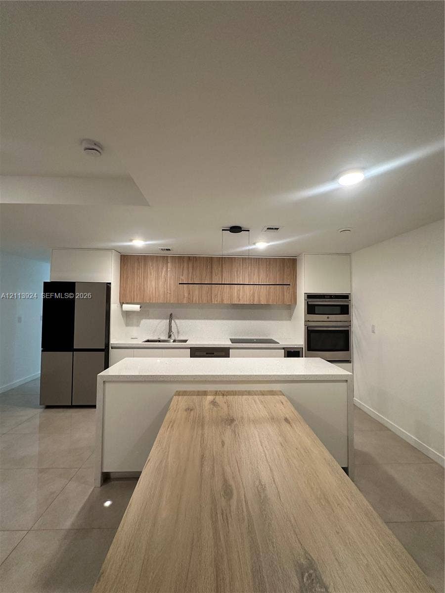 14569 SW 261st Terrace, #14569, Homestead, Homestead, FL 33032 Kitchen featuring dual-tone cabinetry, wood-finish upper cabinets, a waterfall-edge kitchen island, integrated appliances, and large-format tile flooring