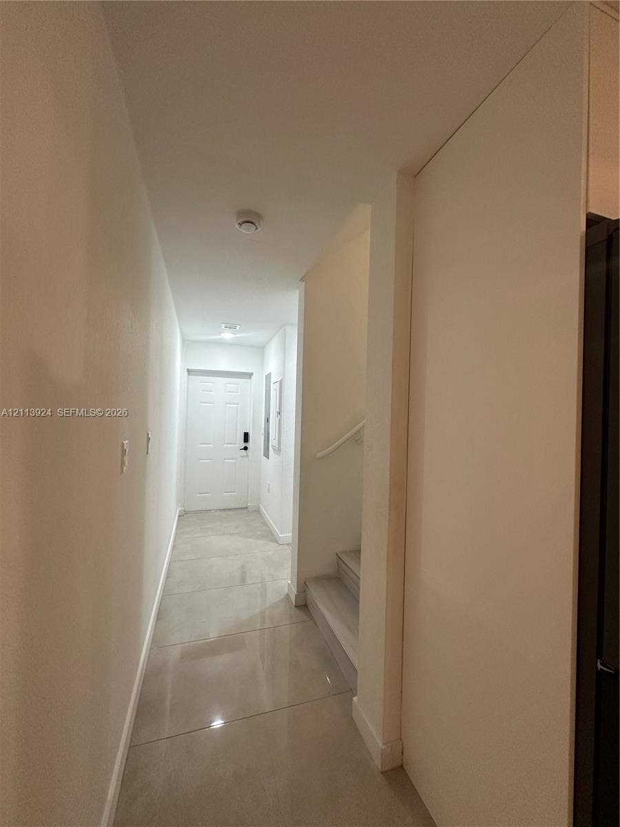 14569 SW 261st Terrace, #14569, Homestead, Homestead, FL 33032 Hallway featuring large-format tile flooring, a six-panel exterior entry door, and a staircase with a mounted handrail