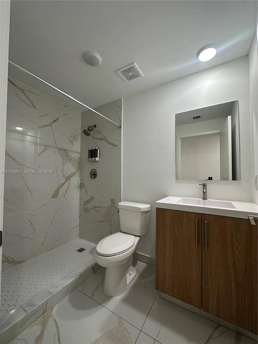 14569 SW 261st Terrace, #14569, Homestead, Homestead, FL 33032 Bathroom featuring a walk-in shower with stone-patterned tile surround, wood-finish vanity with an integrated basin, frameless mirror, and large-format tile flooring