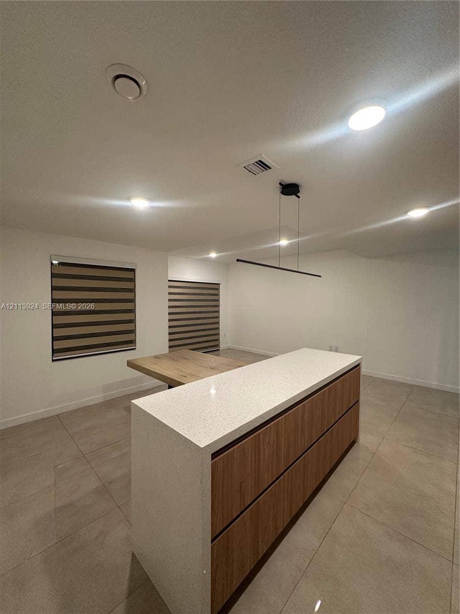14569 SW 261st Terrace, #14569, Homestead, Homestead, FL 33032 Center island featuring a stone-look countertop, wood-finish cabinetry, built-in dining surface, recessed lighting, and modern linear pendant fixture