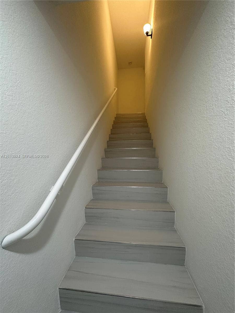 14569 SW 261st Terrace, #14569, Homestead, Homestead, FL 33032 Staircase featuring wood-finish treads, a white wall-mounted handrail, textured wall surfaces, and an attached wall sconce