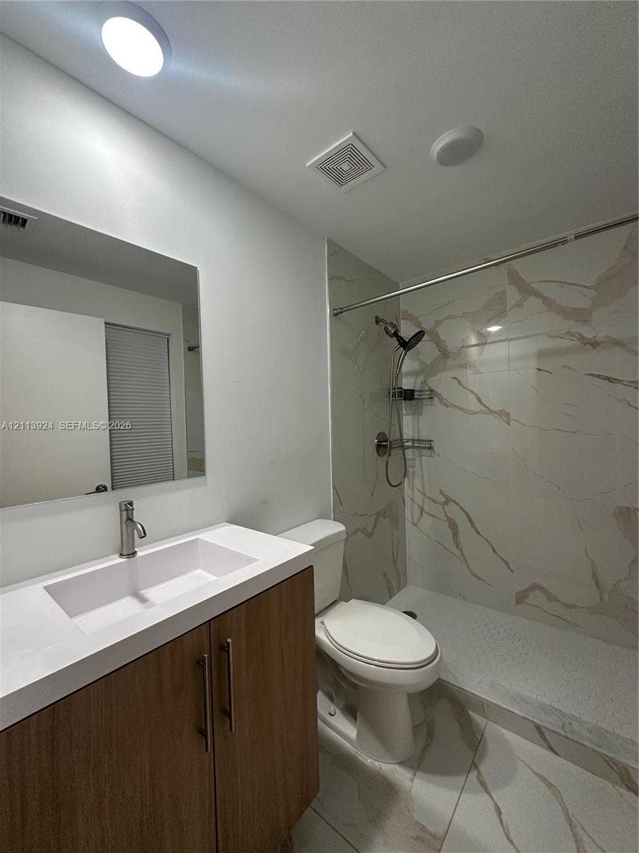 14569 SW 261st Terrace, #14569, Homestead, Homestead, FL 33032 Bathroom featuring a wood-finish vanity with a white countertop and integrated sink, walk-in shower with floor-to-ceiling stone-patterned tile, and large-format tile flooring