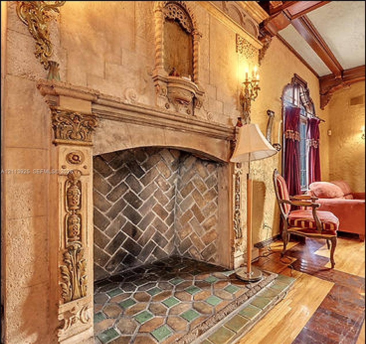 1055 Hollywood Boulevard, Hollywood, Hollywood, FL 33019 Ornate fireplace featuring carved masonry detailing, a herringbone-pattern firebox, decorative tile hearth, and wood-beam ceiling