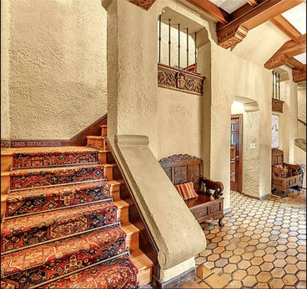 1055 Hollywood Boulevard, Hollywood, Hollywood, FL 33019 Staircase featuring wood treads and exposed ceiling beams, accented by detailed masonry archways and decorative carved wood trim, complemented by hexagonal terracotta tile flooring