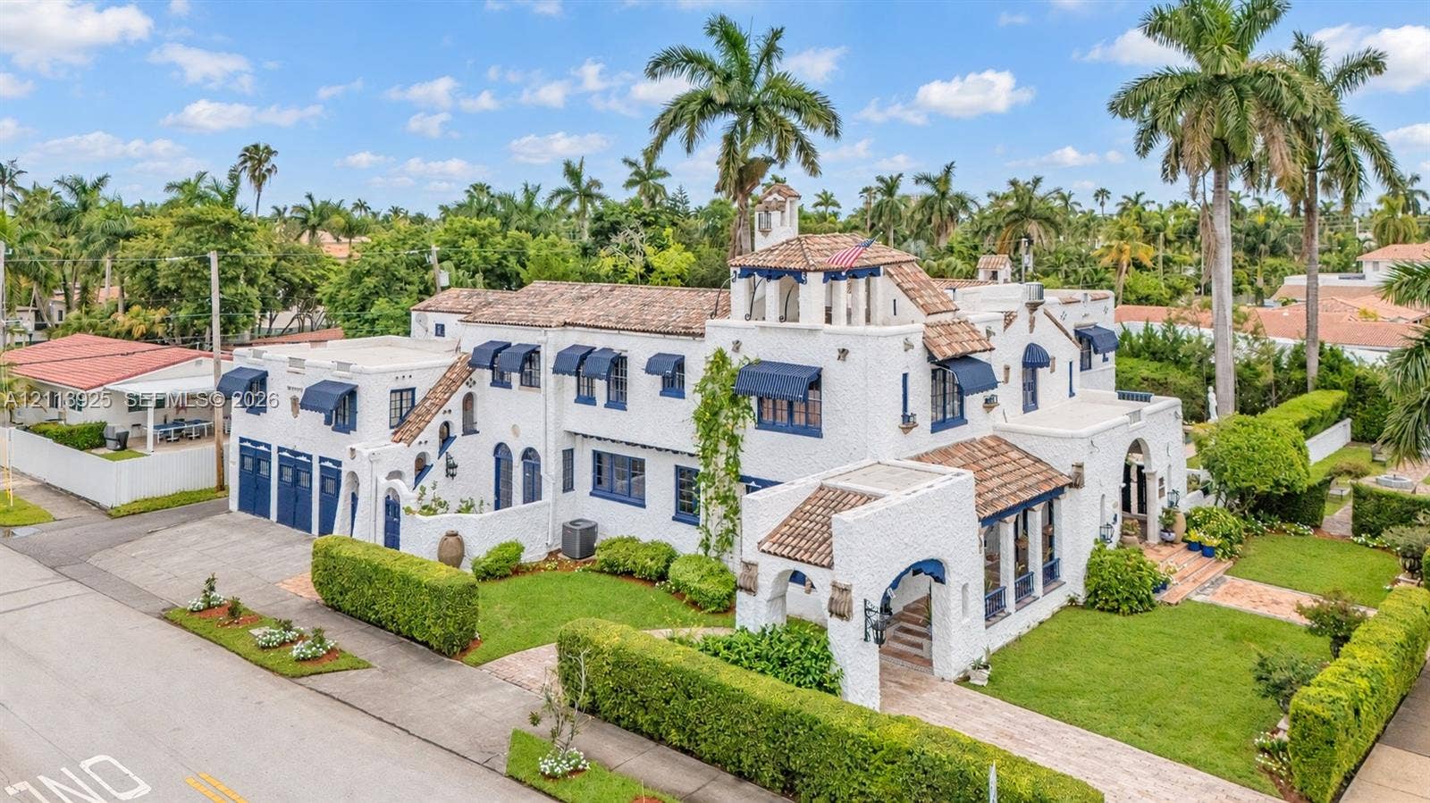 1055 Hollywood Boulevard, Hollywood, Hollywood, FL 33019 Spanish Colonial Revival exterior featuring a multi-level silhouette, textured white masonry, clay tile roofing, arched entryway, and blue metal window awnings