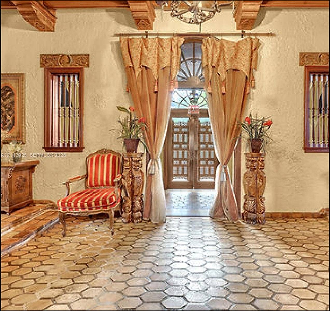 1055 Hollywood Boulevard, Hollywood, Hollywood, FL 33019 Entryway featuring hexagonal terracotta floor tiling, decorative wooden ceiling beams, dual casement windows with intricate carved wood surrounds, and a central arched entryway with decorative transom glass