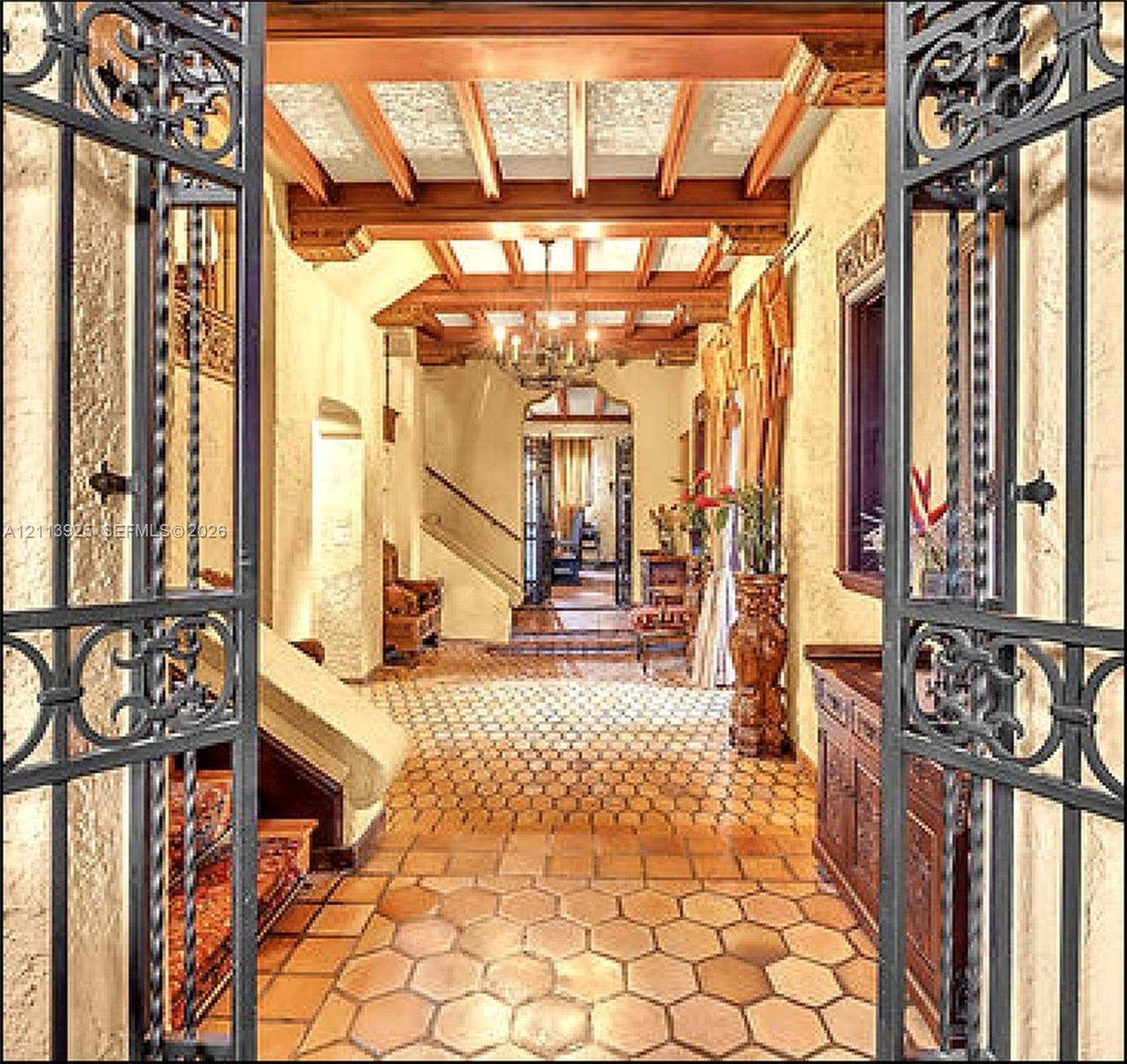 1055 Hollywood Boulevard, Hollywood, Hollywood, FL 33019 Foyer featuring intricate wrought-iron gate entry, hexagonal terracotta tile flooring, exposed beamed ceiling with decorative millwork, and a wrought-iron chandelier