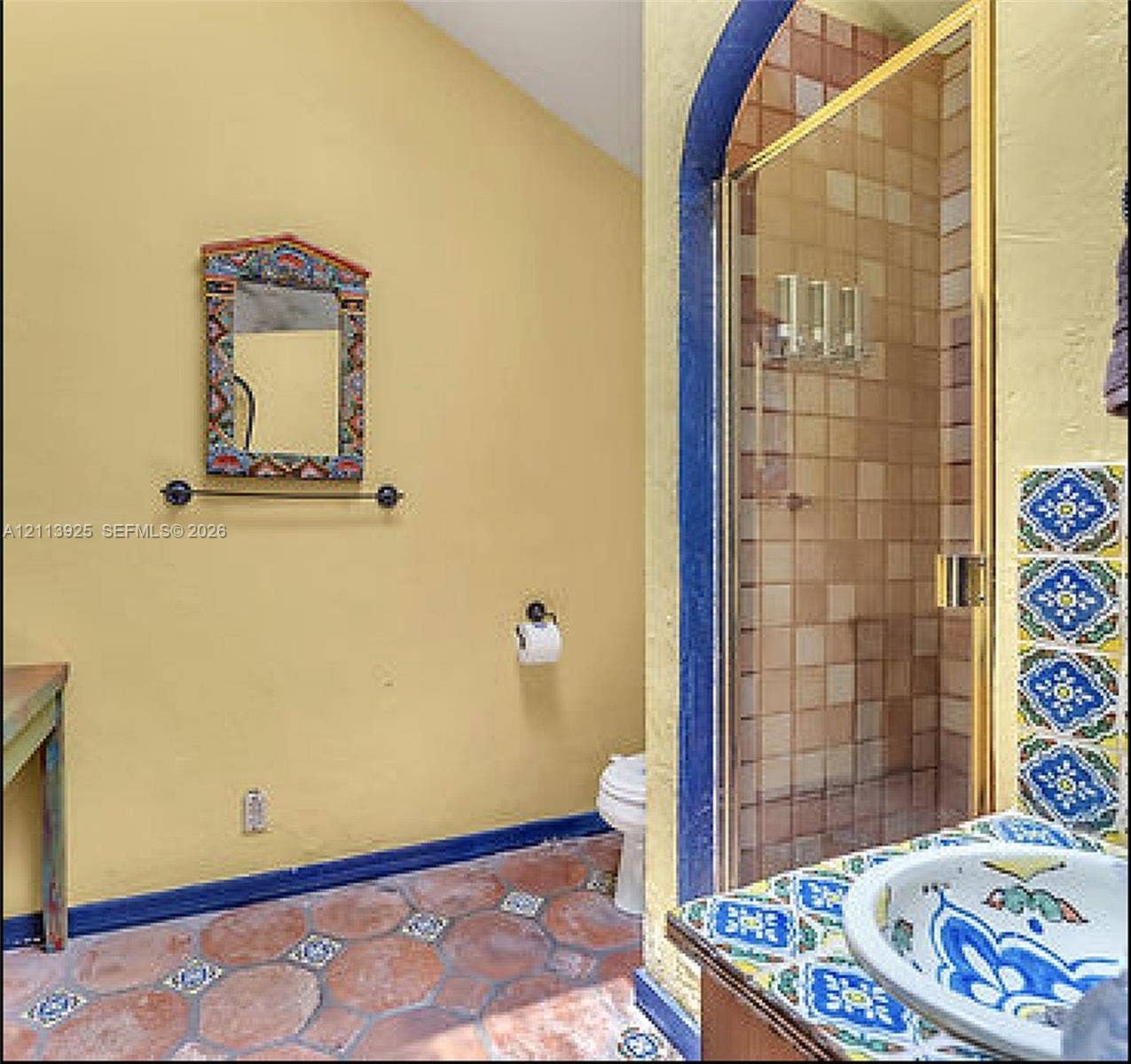 1055 Hollywood Boulevard, Hollywood, Hollywood, FL 33019 Bathroom featuring custom hand-painted ceramic tile accents, arched shower entry, terracotta tile flooring with inlaid decorative inserts, and a painted wood-frame wall mirror