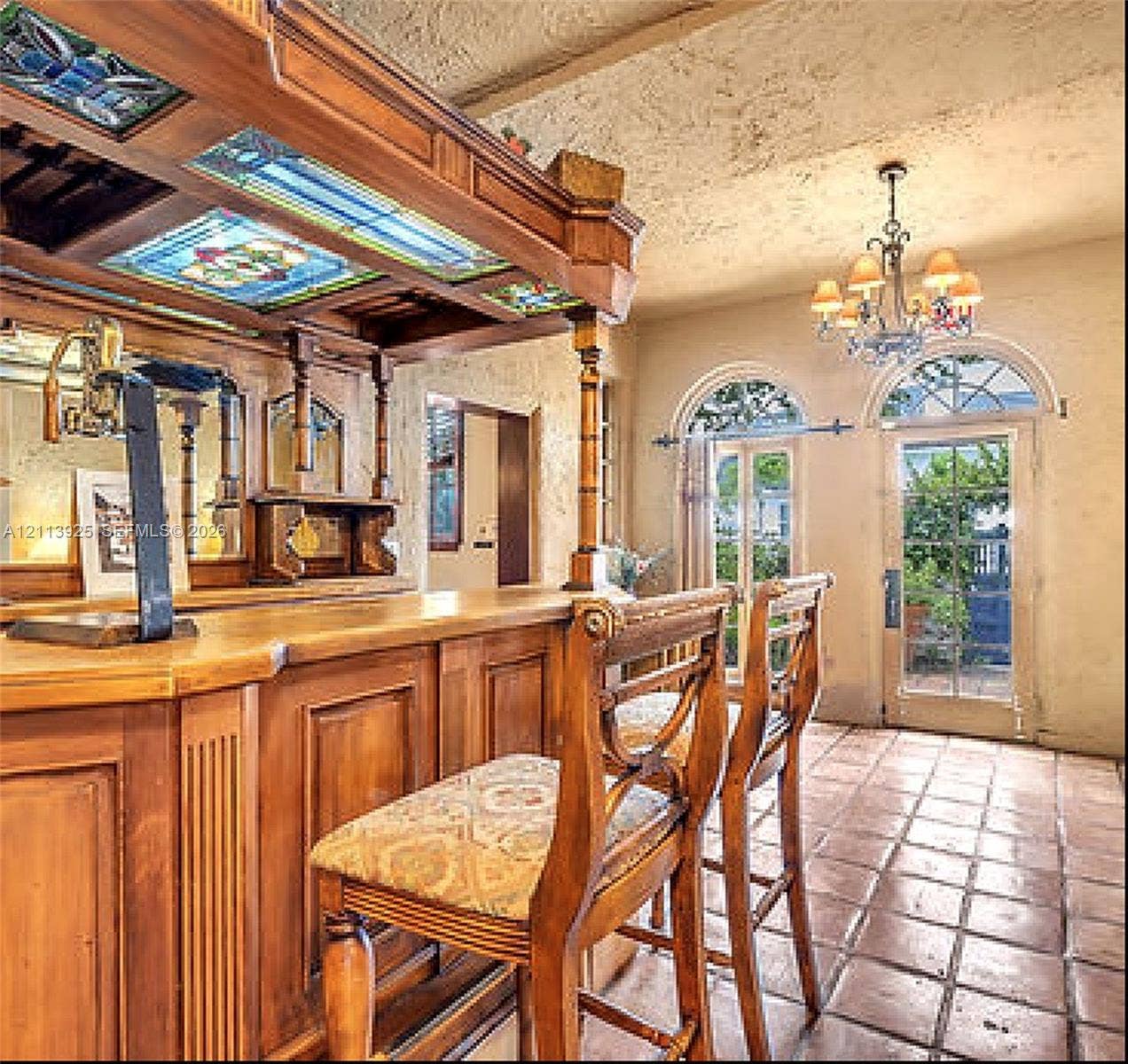 1055 Hollywood Boulevard, Hollywood, Hollywood, FL 33019 Custom wood-paneled bar featuring stained glass ceiling insets, ornate millwork, tiled flooring, arched glass-paneled doors, and a multi-tiered chandelier