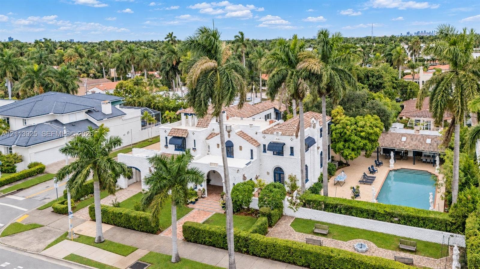 1055 Hollywood Boulevard, Hollywood, Hollywood, FL 33019 Spanish Colonial-style exterior with white stucco facade, tile roofing, arched entryway, private swimming pool, and landscaped grounds featuring mature palm trees