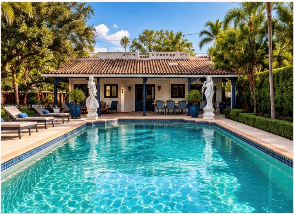 1055 Hollywood Boulevard, Hollywood, Hollywood, FL 33019 In-ground pool with decorative statues, expansive stone-paved patio, covered veranda featuring dark structural columns, and clay tile roof