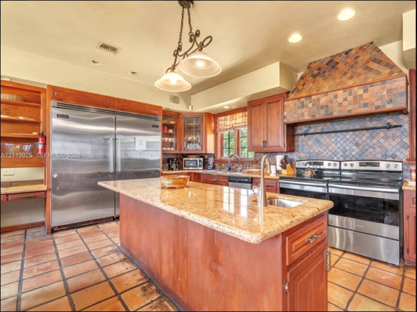 1055 Hollywood Boulevard, Hollywood, Hollywood, FL 33019 Kitchen featuring a large central island with stone-finish countertops, stainless steel appliances, custom wood cabinetry, a decorative tiled range hood, and terra cotta floor tiles