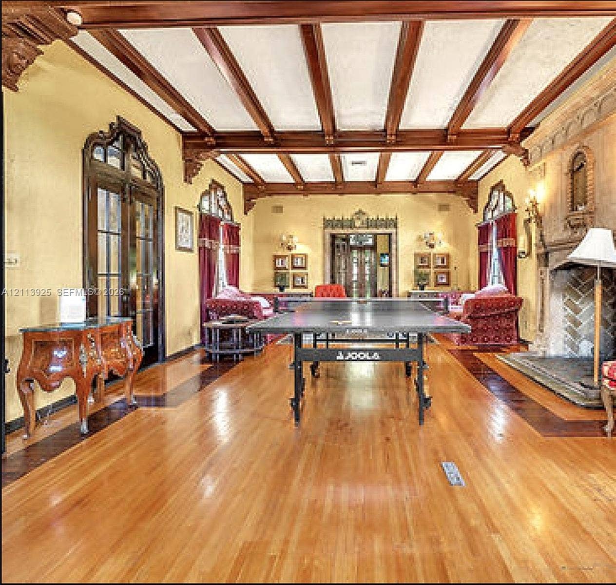 1055 Hollywood Boulevard, Hollywood, Hollywood, FL 33019 Expansive room featuring dark-stained wood ceiling beams, decorative corbels, wood-finish flooring with contrasting inlay borders, arched glass-paneled doors, and a floor-to-ceiling stone fireplace