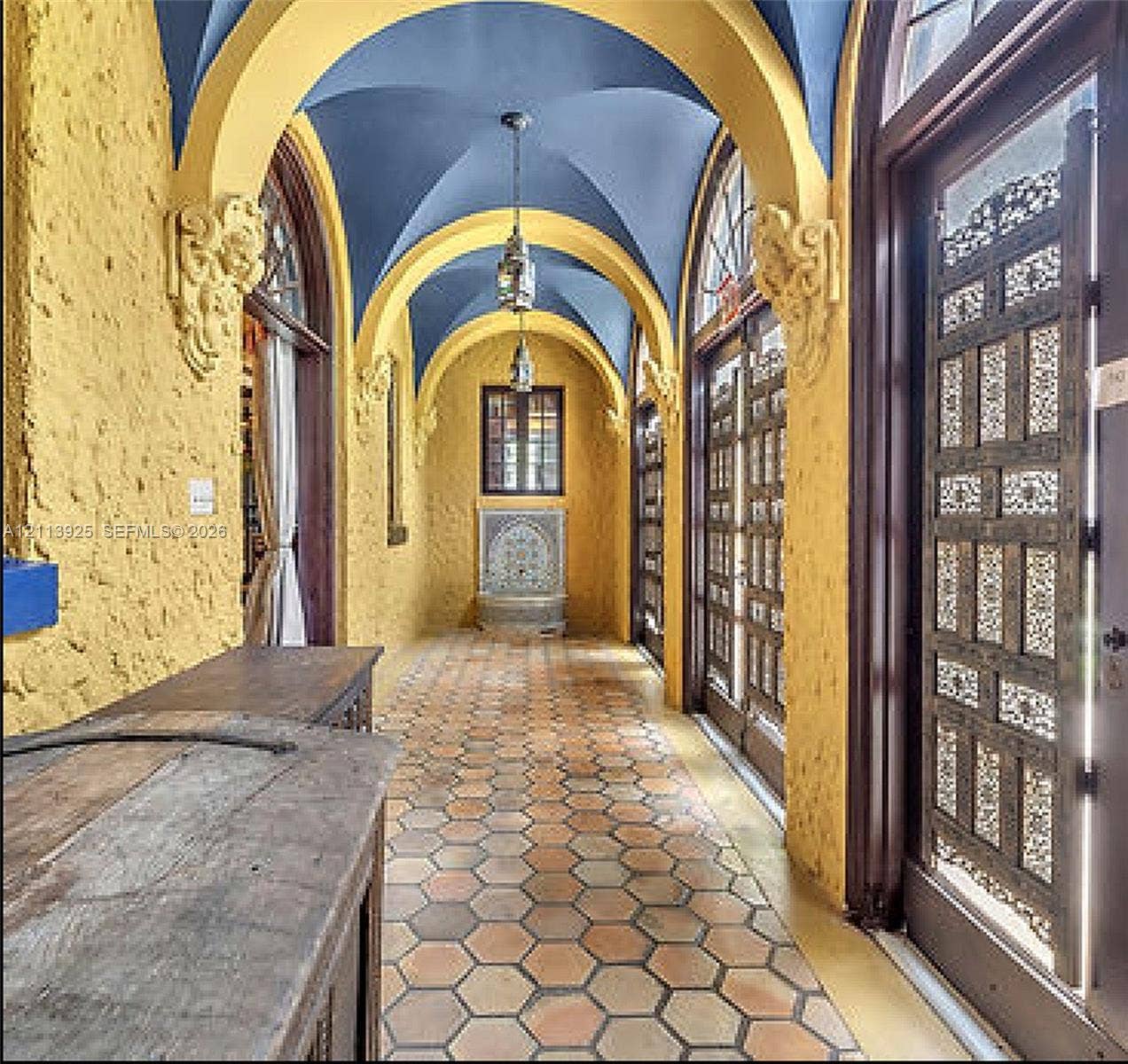 1055 Hollywood Boulevard, Hollywood, Hollywood, FL 33019 Vaulted corridor featuring a blue barrel-vaulted ceiling, decorative corbels, hexagonal terracotta tile flooring, ornate latticework doors, and an arched stone wall fountain
