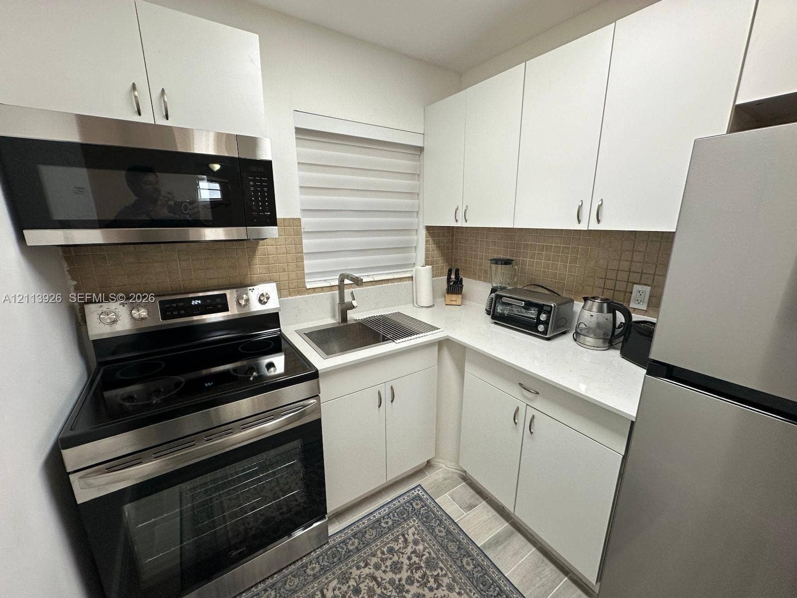 2008 Jackson Street, #D3, Hollywood, FL 33020 Kitchen featuring white cabinetry, light-toned stone-style countertops, stainless steel appliances, a textured tile backsplash, and a stainless steel undermount sink with a gooseneck faucet