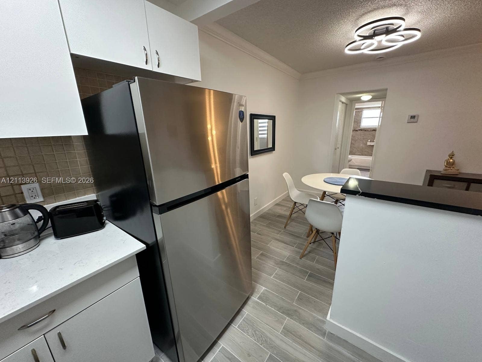 2008 Jackson Street, #D3, Hollywood, FL 33020 Kitchen featuring white cabinetry, solid-surface countertops, tile backsplash, stainless steel refrigerator, and wood-finish flooring