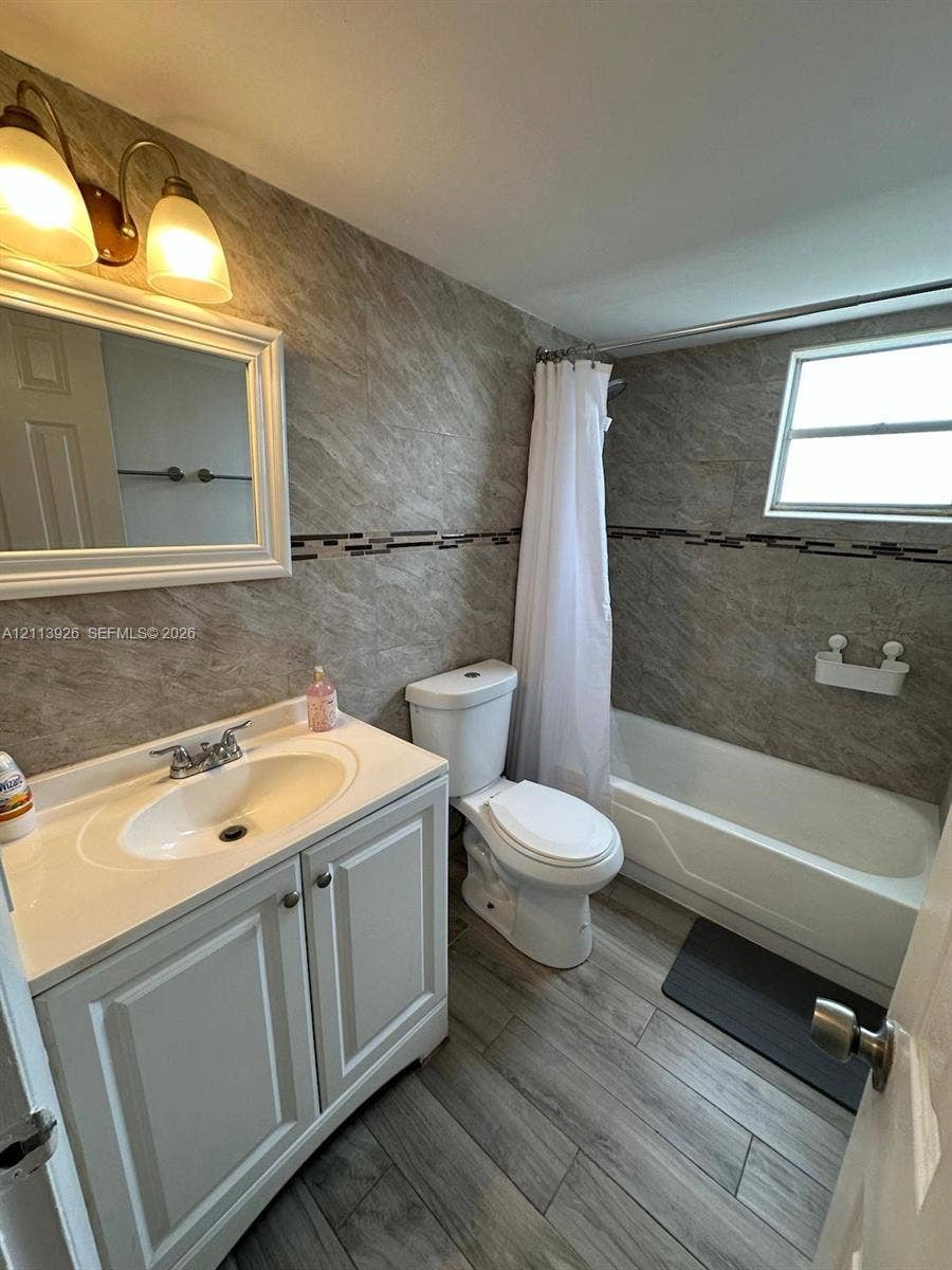 2008 Jackson Street, #D3, Hollywood, FL 33020 Bathroom featuring wood-finish flooring, a white vanity with a molded basin, stone-finish wall tile, a decorative glass tile accent border, and a tub-shower combination