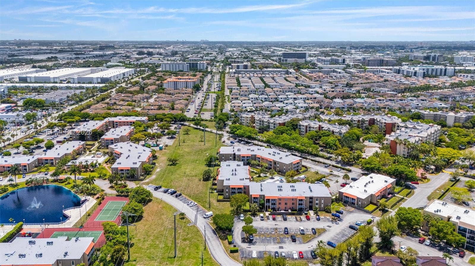4900 NW 79th Avenue, #202, Doral, Doral, FL 33166 Aerial perspective featuring multi-story residential buildings, a central water feature with a fountain, paved surface parking, and tennis courts