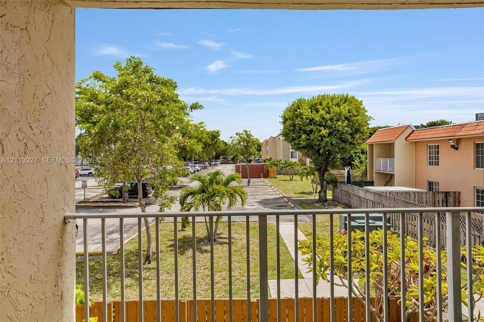 4900 NW 79th Avenue, #202, Doral, Doral, FL 33166 Balcony featuring metal railing and stucco pillar finish, overlooking exterior grounds with mature landscaping and paved parking area