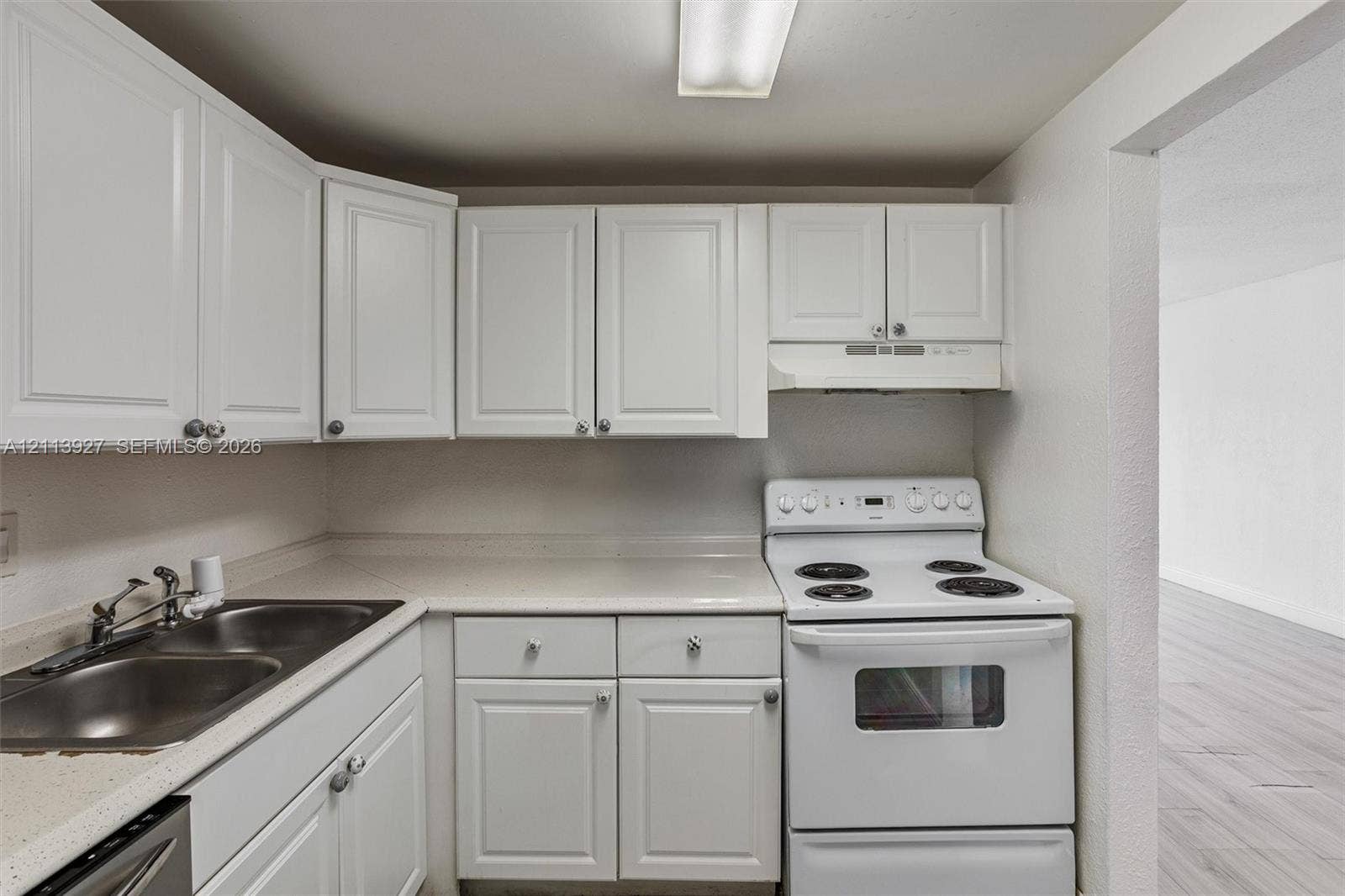 4900 NW 79th Avenue, #202, Doral, Doral, FL 33166 Kitchen featuring white shaker-style cabinetry, solid-surface countertops, dual-basin stainless steel sink, and a white electric range with an integrated hood