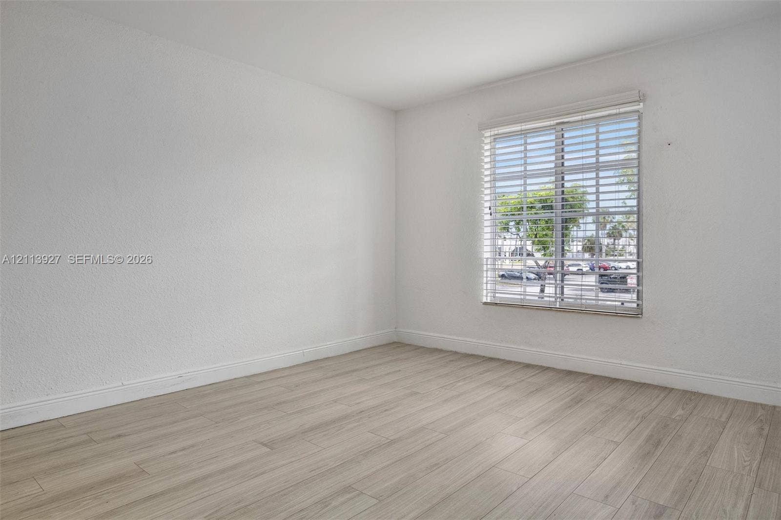 4900 NW 79th Avenue, #202, Doral, Doral, FL 33166 Neutral interior space featuring wood-finish flooring, crisp white walls, and a large window equipped with horizontal slat blinds