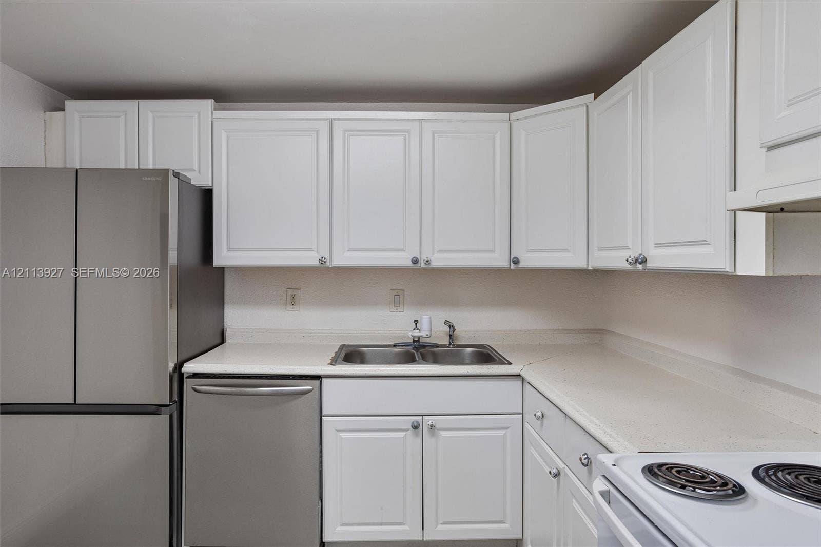 4900 NW 79th Avenue, #202, Doral, Doral, FL 33166 Kitchen featuring white shaker-style cabinetry, solid-surface countertops, dual-basin stainless steel sink, and stainless steel appliances