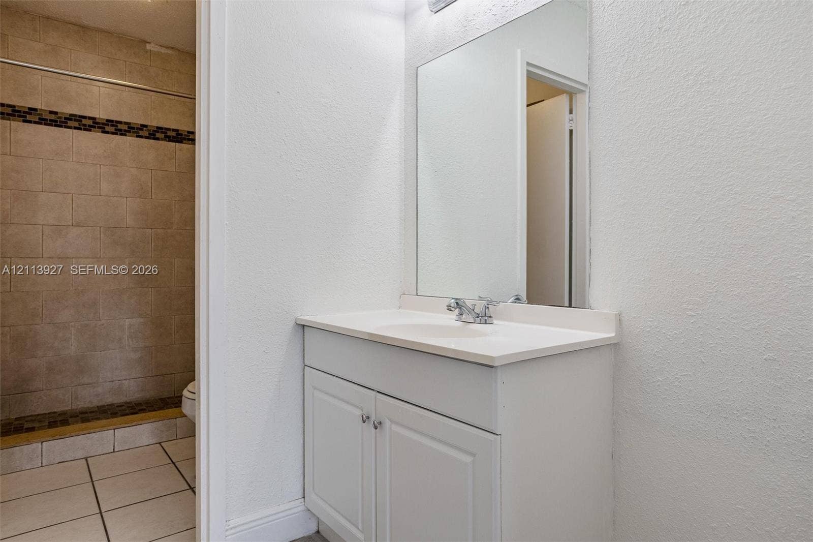 4900 NW 79th Avenue, #202, Doral, Doral, FL 33166 Bathroom featuring a white vanity with an integrated sink, polished chrome faucet, expansive wall-mounted mirror, and a walk-in shower with neutral stone-finish tile surround and decorative accent inlay
